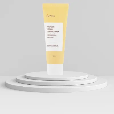 A yellow tube of IUNIK Propolis Vitamin Sleeping Mask is displayed on a white tiered stand against a light gray background.