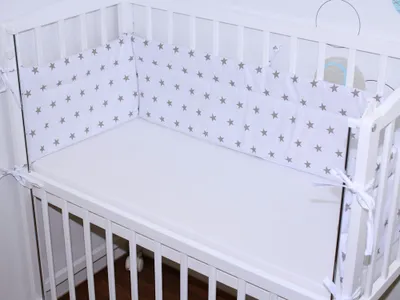 A close-up view of a baby crib with a white mattress and a white bumper pad decorated with gray stars.