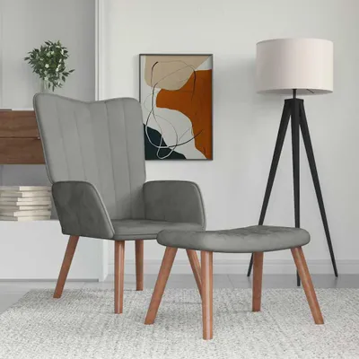 A grey velvet armchair and ottoman are placed on a rug in a room with a floor lamp and abstract art on the wall.