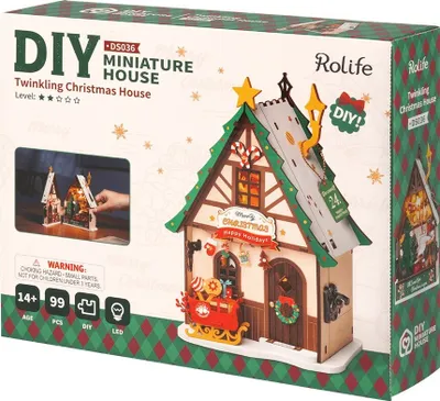 The image shows the packaging of a DIY miniature Christmas house kit. The packaging features a prominent image of the assembled house, along with product details and branding.