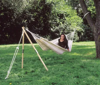 A woman relaxing in a hammock supported by a wooden stand and a tree in a grassy outdoor setting.