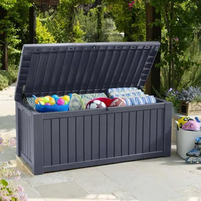 An open storage box filled with outdoor toys and cushions, placed on a patio.