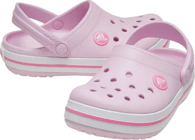 A pair of light pink Crocs with white and pink stripes on the sole, shown from a slightly elevated angle against a white background.