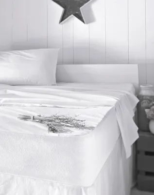 A white mattress protector is shown on a bed with a pillow and a small bunch of dried lavender.