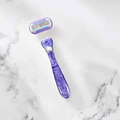 A purple Gillette Venus razor and its replacement head are displayed on a marble-like surface.