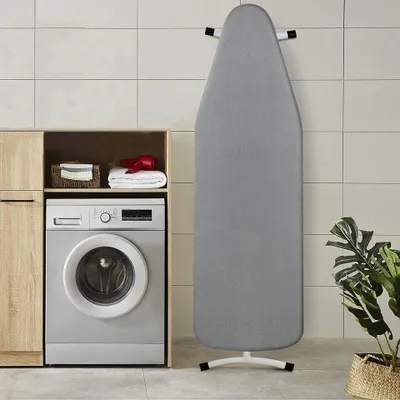 A laundry room scene with a washing machine, cabinets, and an ironing board.