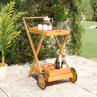 A wooden serving cart is placed on a stone patio, surrounded by greenery and a lawn.