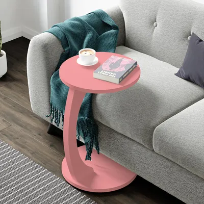 A pink C-shaped side table next to a light gray sofa, with a teal throw blanket and a cup of coffee on top.