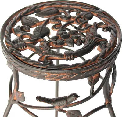 A close-up view of a decorative metal plant stand with intricate floral and bird motifs.