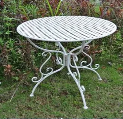 A white metal garden table with a perforated top and ornate legs sits on grass and foliage.