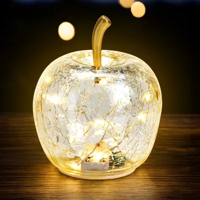 A decorative glass apple with embedded LED lights sits on a wooden surface.