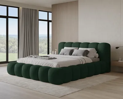 A bedroom scene with a large green bed as the focal point, positioned in front of large windows with a view of trees and hills.