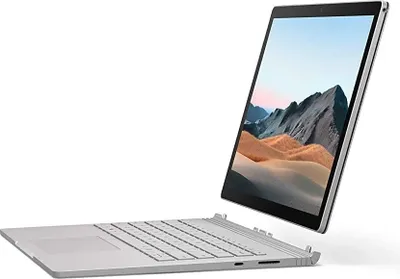 A silver Microsoft Surface Book 2 laptop is shown at an angle against a white background. The screen is open and displays a landscape image.