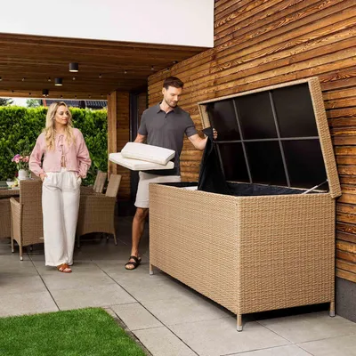 A couple is putting cushions into a large storage box on a patio.