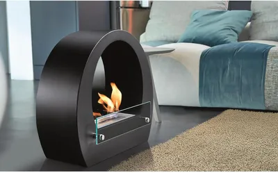 A modern black bioethanol fireplace with a flame is placed on the floor next to a sofa and a rug.