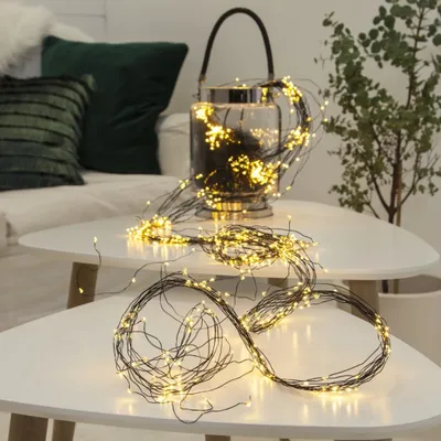 A decorative string of LED lights is draped over two white tables, with a glass lantern containing more lights in the background.