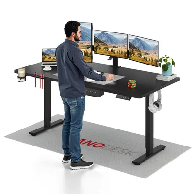 A man stands at a standing desk with multiple monitors, a laptop, and accessories.