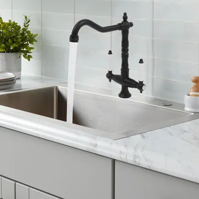 A black faucet with white handles is running water into a stainless steel sink.