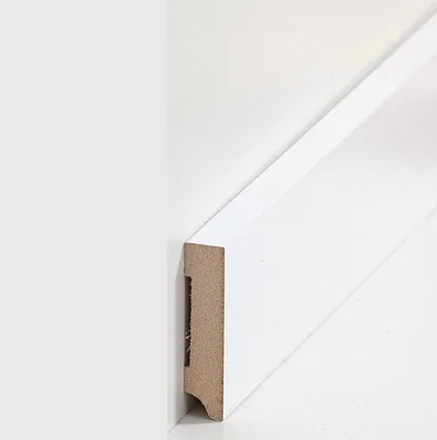 A close-up view of a white MDF baseboard profile against a white wall.