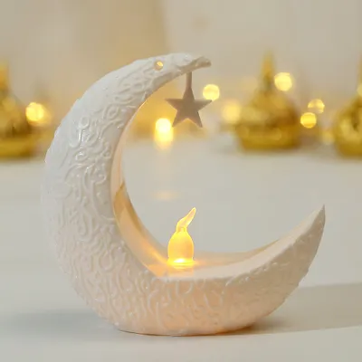 A white crescent moon-shaped LED night light with a small star hanging from the top and a flickering LED candle inside.