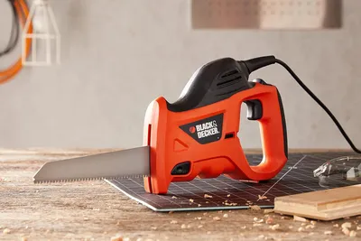 A Black & Decker electric reciprocating saw is placed on a wooden surface with a cutting mat underneath.
