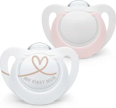 Two NUK pacifiers are shown against a white background. One pacifier is in the foreground and has a heart design and text. The other pacifier is in the background and is pink.