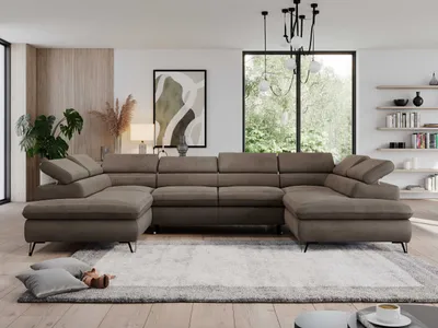 A spacious living room with a large U-shaped sofa, a rug, and a window overlooking greenery.