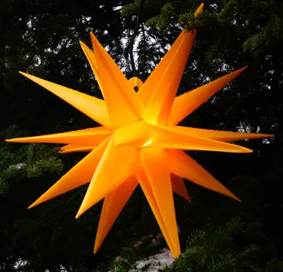 A yellow, star-shaped Christmas decoration hangs from a tree branch.