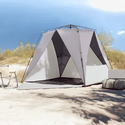 A tent set up on a sandy beach with a chair and duffel bag nearby.