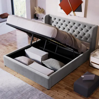 A gray upholstered storage bed with the mattress lifted to reveal storage space underneath, containing boxes and pillows.