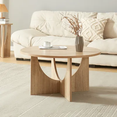 A round coffee table with a vase and cup on it, placed in front of a couch.