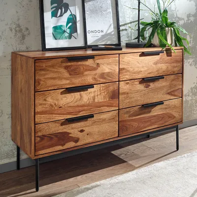 A wooden dresser with six drawers and black metal legs, placed in a room with a textured wall and a rug.