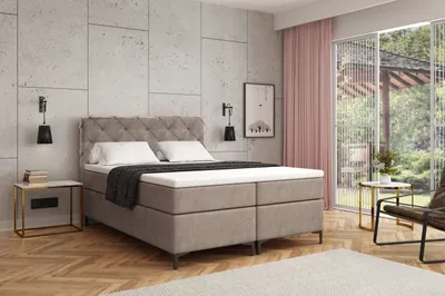 A bedroom scene featuring a boxspring bed, nightstand, chair, and window with curtains.