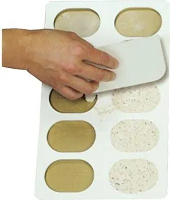 A hand is shown using a white scraper to remove a circular stencil from a tray of baked goods.