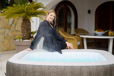 A woman sits on the edge of an inflatable hot tub on a patio.