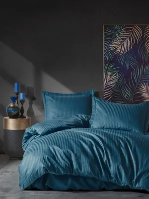A neatly made bed with blue bedding, a bedside table with decorative items, and a framed artwork on the wall.