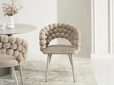 A beige dining chair with a unique bubble-like backrest is shown in a well-lit room, next to a round table with a vase of flowers.