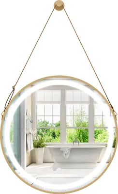 A round bathroom mirror with LED lighting, suspended by a strap, reflecting a bathroom interior with a bathtub and window.