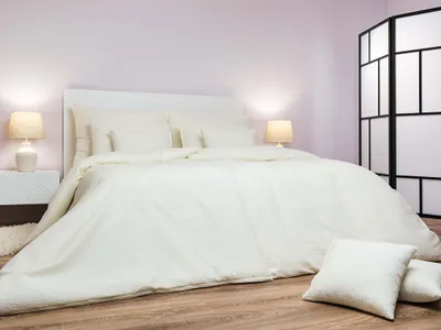 A neatly made bed with white bedding in a room with a light purple wall.