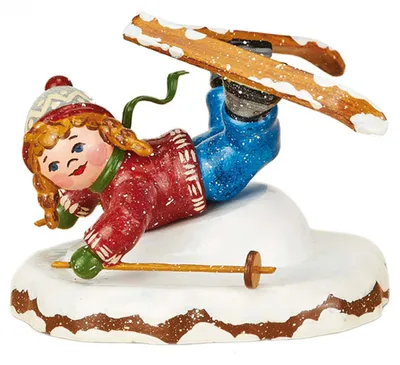 Ein fröhliches Kind mit roten Wangen und Zöpfen trägt einen roten Pullover und blaue Hosen während es auf Skiern eine Bauchlandung im Schnee macht und dabei lächelt