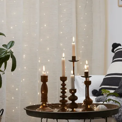 Candles on a tray in front of a curtain with fairy lights.