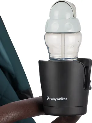 A close-up of a black cup holder with a baby bottle inside, attached to a stroller handle.