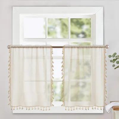 Two sheer curtains with tassels hanging on a window rod in front of a window.