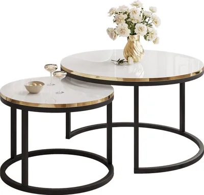 Two nesting round coffee tables with white tops and gold trim, on black metal bases. A vase of white flowers and two wine glasses are on the smaller table.