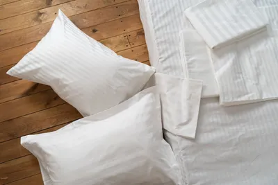 A top-down view of white striped bedding and pillows arranged on a wooden floor.