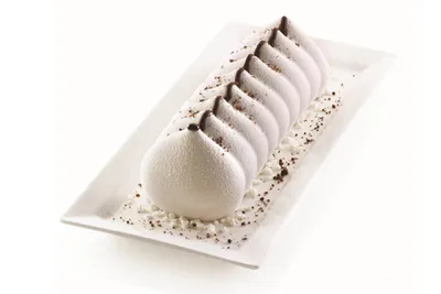 A white silicone mold for making desserts, presented on a white rectangular plate with chocolate crumbs.