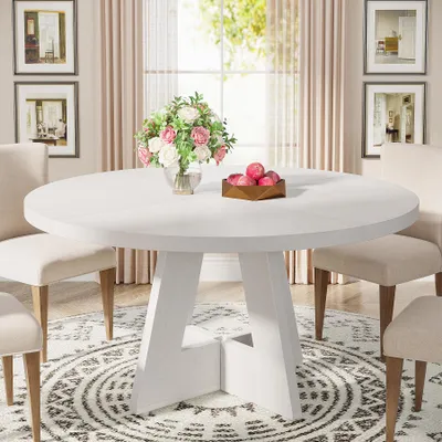 A white round dining table with chairs around it, set in a dining room with artwork on the wall and curtains in the background.