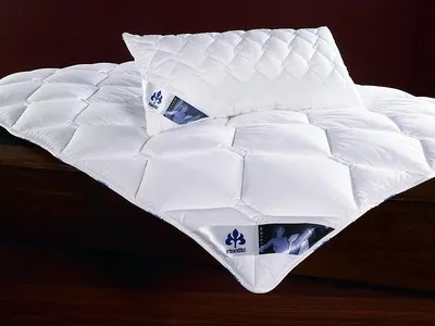 A white quilted duvet and pillow are laid out on a dark wooden surface.