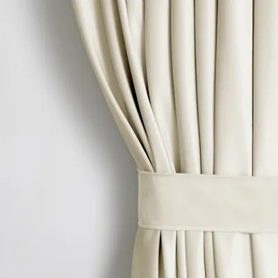A close-up view of a cream-colored velvet curtain, showing its texture and pleats, with a tie-back band.