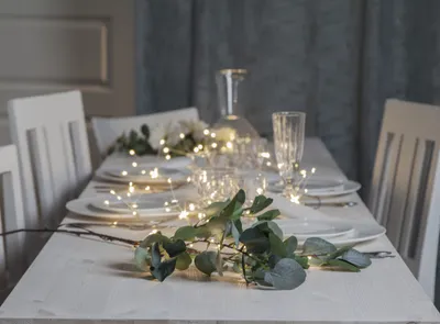 A beautifully set table with white plates, cutlery, and a decorative branch with LED lights and eucalyptus leaves.